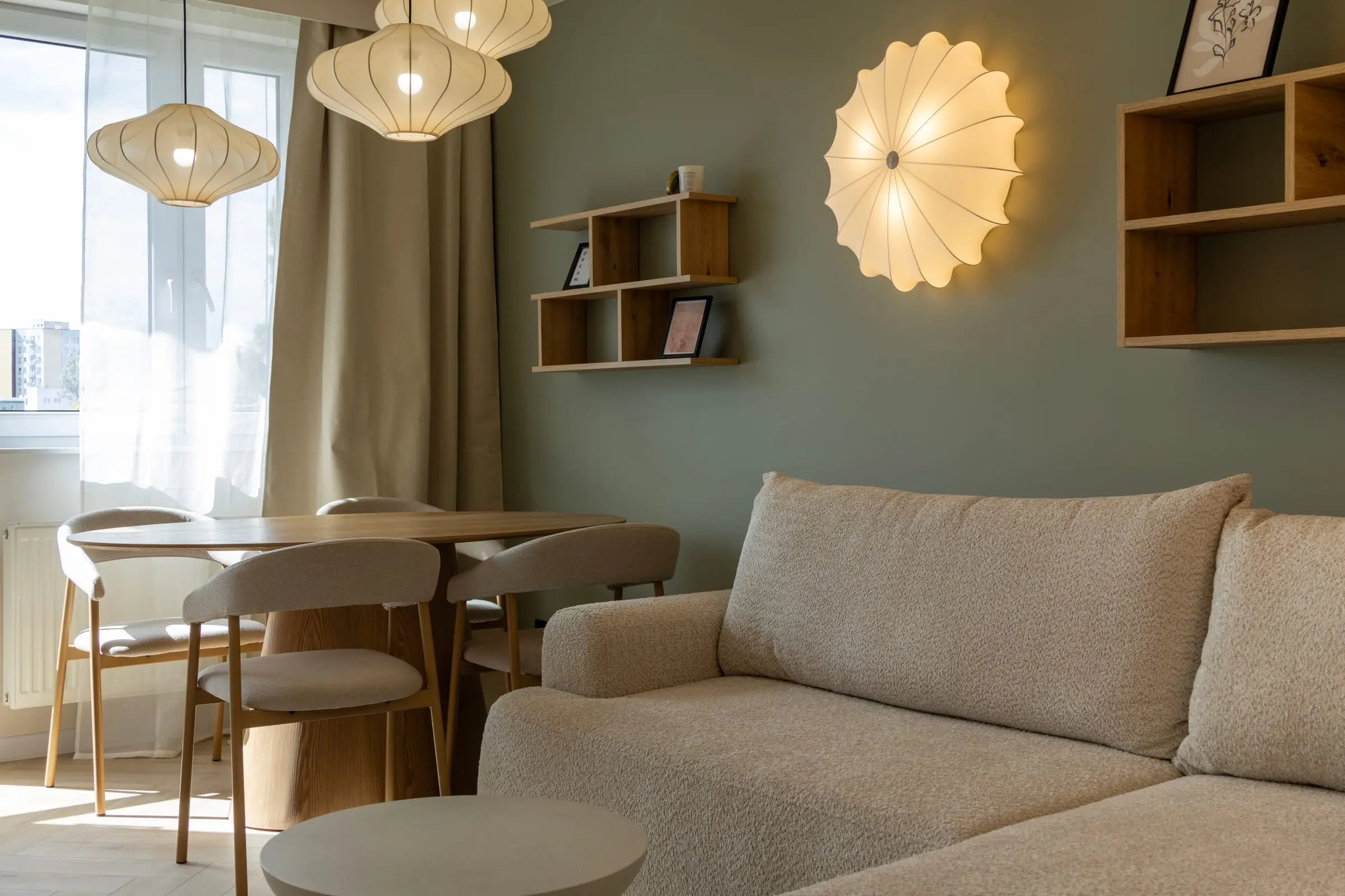 Wykończony salon z jadalnią i szałwiową ścianą, ciepłe światło dekoracyjnych lamp — remont mieszkania